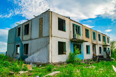 View of an old brick dilapidated building without a roof on green grass against a blue cloudy sky