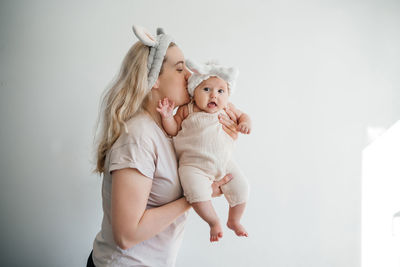 Mom blonde and newborn daughter in white with rabbit ears photo on a light background