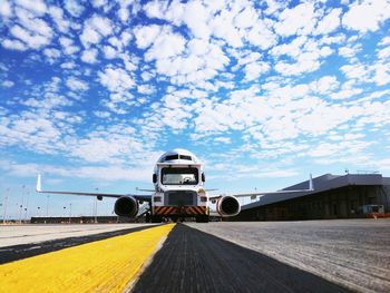 Truck and airplane on runway at airport against sky