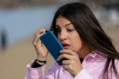 Outdoors portrait of young beautiful teen using smartphone as mirror while do her makeup 