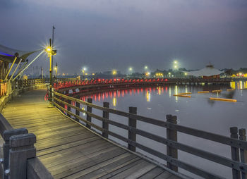 Illuminated footbridge over lake against sky during night