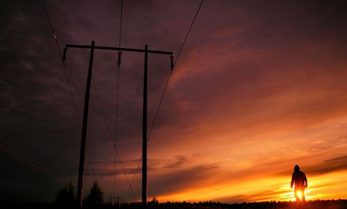 Silhouette electricity pylon against dramatic sky during sunset