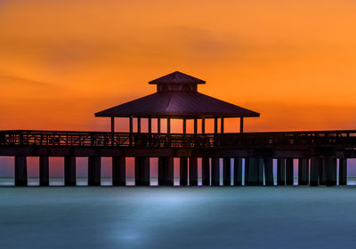 Built structure on pier over sea against orange sky during sunset