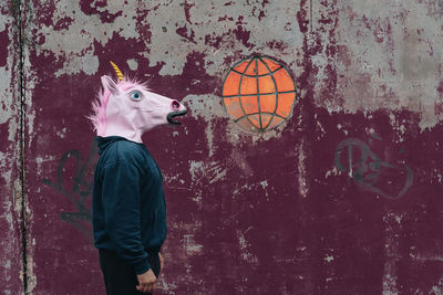 Side view of man wearing horse mask while standing against wall