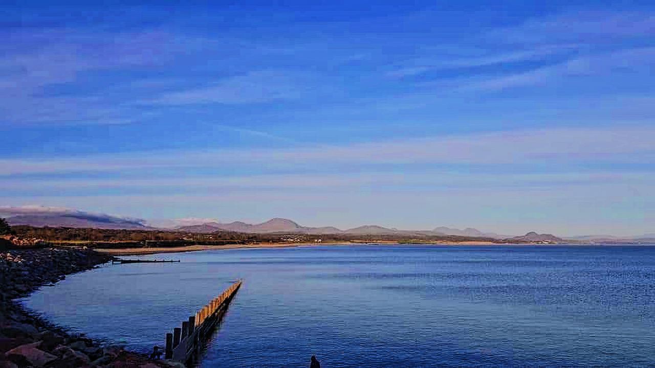 SCENIC VIEW OF SEA BY MOUNTAINS AGAINST BLUE SKY