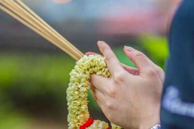 Cropped hands of woman holding incense sticks with floral garland in temple