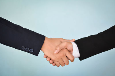Cropped image of business people giving handshake against blue background