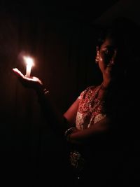Woman holding lit candle in dark