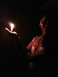 Midsection of man holding lit candle in dark