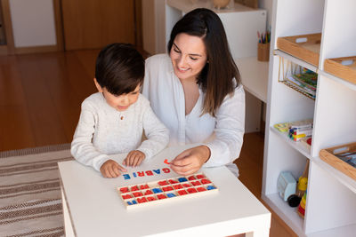 Mother assisting son in puzzle sitting at home