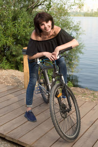 The smiling brunette stopped to rest on riverbank while riding a bike.