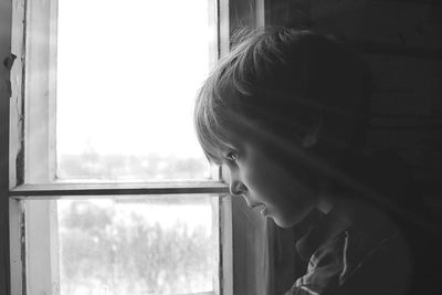 Close-up of cute boy looking through window at home