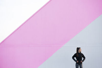 Young woman standing against pink wall