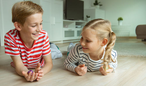 Cheerful siblings playing with dice while lying on carpet at home