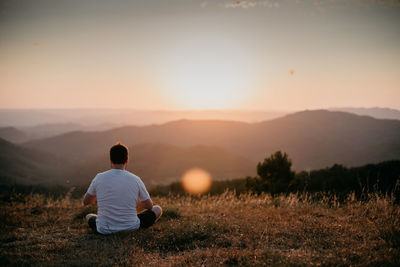 Rear view of man sitting on field at sunset