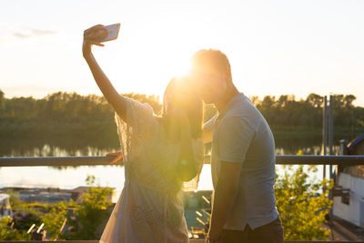 Rear view of woman photographing on mobile phone against sky