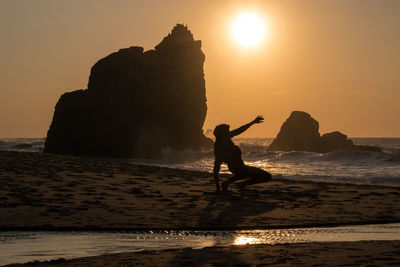 Silhouette man standing on rock at beach against clear sky