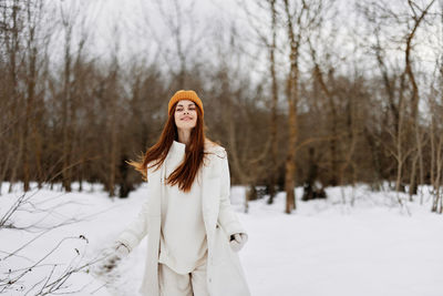 Portrait of young woman standing on snow covered field during winter