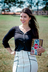 Smiling young woman holding book while standing outdoors