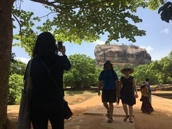 Rear view of man photographing woman using smart phone against sky