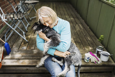 Happy senior woman embracing dog while sitting on porch