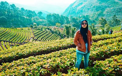 Portrait of smiling young woman standing on field against mountain