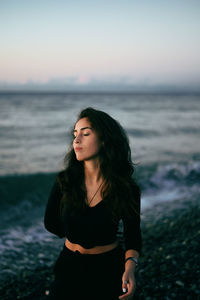 Beautiful young woman standing at sea shore against sky