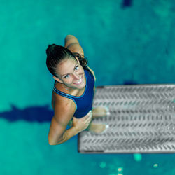 High angle portrait of smiling swimmer standing on diving platform over swimming pool