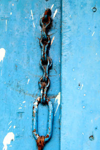 Close-up of rusty metal chain against blue wall