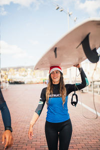 Smiling young woman carrying surfboard on head in city