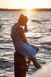 Side view of woman standing at beach during sunset