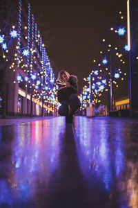 Surface level of woman crouching on footpath against sky at night