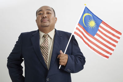 Portrait of businessman holding malaysia flag against wall