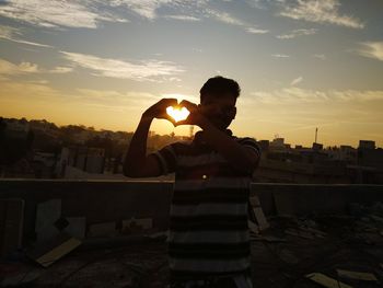 Man standing by cityscape against sky during sunset