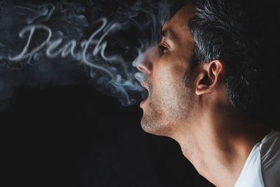 Close-up of man exhaling smoke against black background