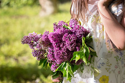 Midsection of girl holding pink flowers while standing in yard