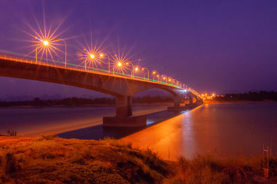 Illuminated bridge over river against sky at night