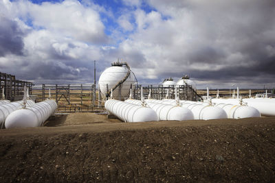 Storage tank at power station against cloudy sky