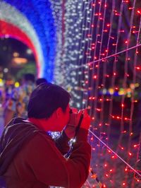 Side view of mid adult woman photographing illuminated lights at night