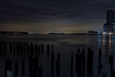 Illuminated city by river against sky at sunset