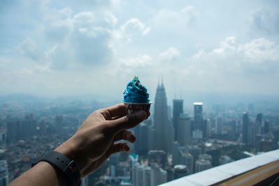 Close-up of man holding cupcake  against cityscape