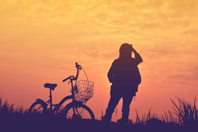 Silhouette person with bicycle against sky during sunset