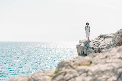 Man standing on rock by sea against clear sky