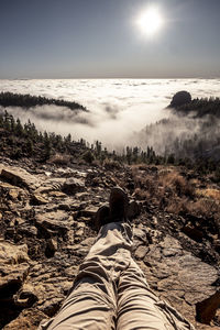 Low section of man sitting on rock against fog and sky