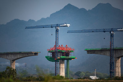 Cranes on bridge against sky