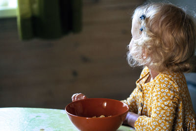 Close-up of girl with bowl on table at home