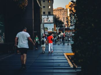 Rear view of people walking on footpath in city