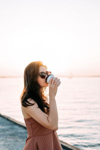 Young woman wearing sunglasses standing against sea