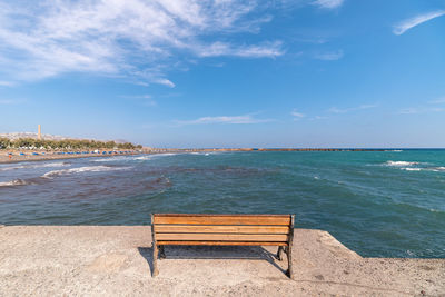 Empty bench on beach by sea against sky