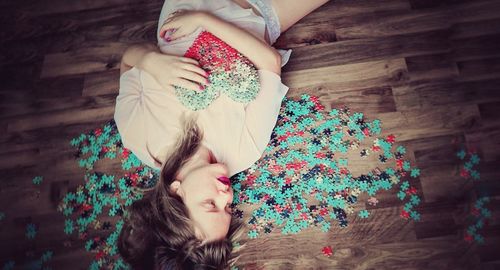 High angle view of woman lying down amidst jigsaw pieces on hardwood floor